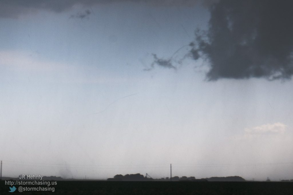 First tornado of the day becomes visible to our southwest as we blast east to escape the hail core. Only a very thin rope is seen, and the debris cloud on the ground is far removed from the base of the supercell. - 6/20/2011 5:26:54 PM - 4 miles southeast of Hampton, NE - Hampton, NE - 